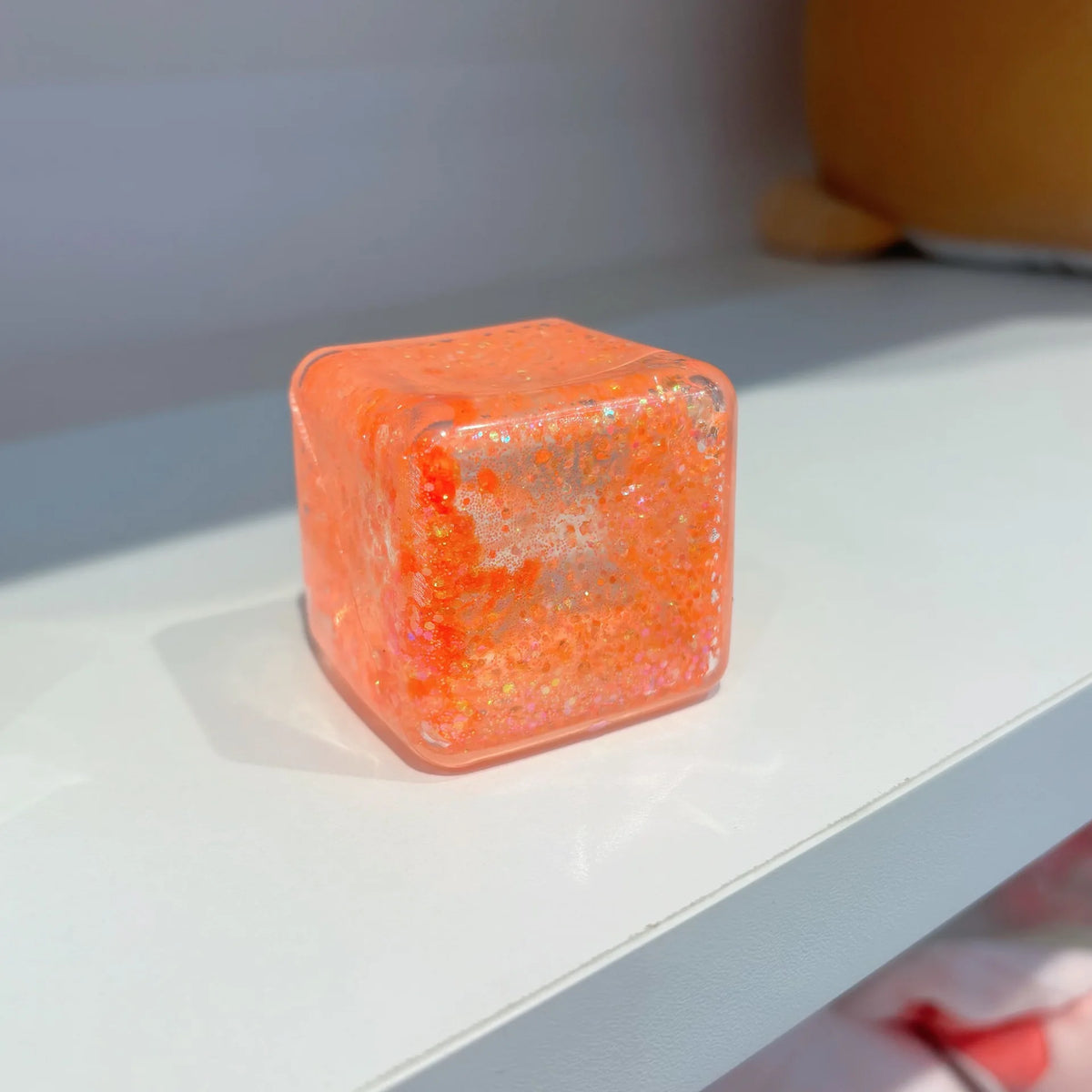 Oranges quadratisches Stressabbau-Fidget-Spielzeug auf einer weißen Oberfläche.