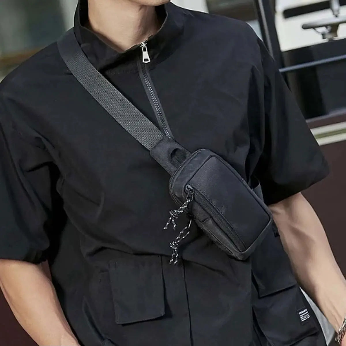 A person wearing a black short-sleeved shirt with a canvas crossbody bag attached to the shirt.