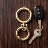 A set of round gold spring snap hooks and a key with a black fob are displayed on dark wood.