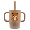 A beige silicone training cup for babies featuring a cute orange bear design, complete with a straw and handles.