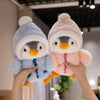 Two adorable penguin plush toys wearing knitted hats being held by hands