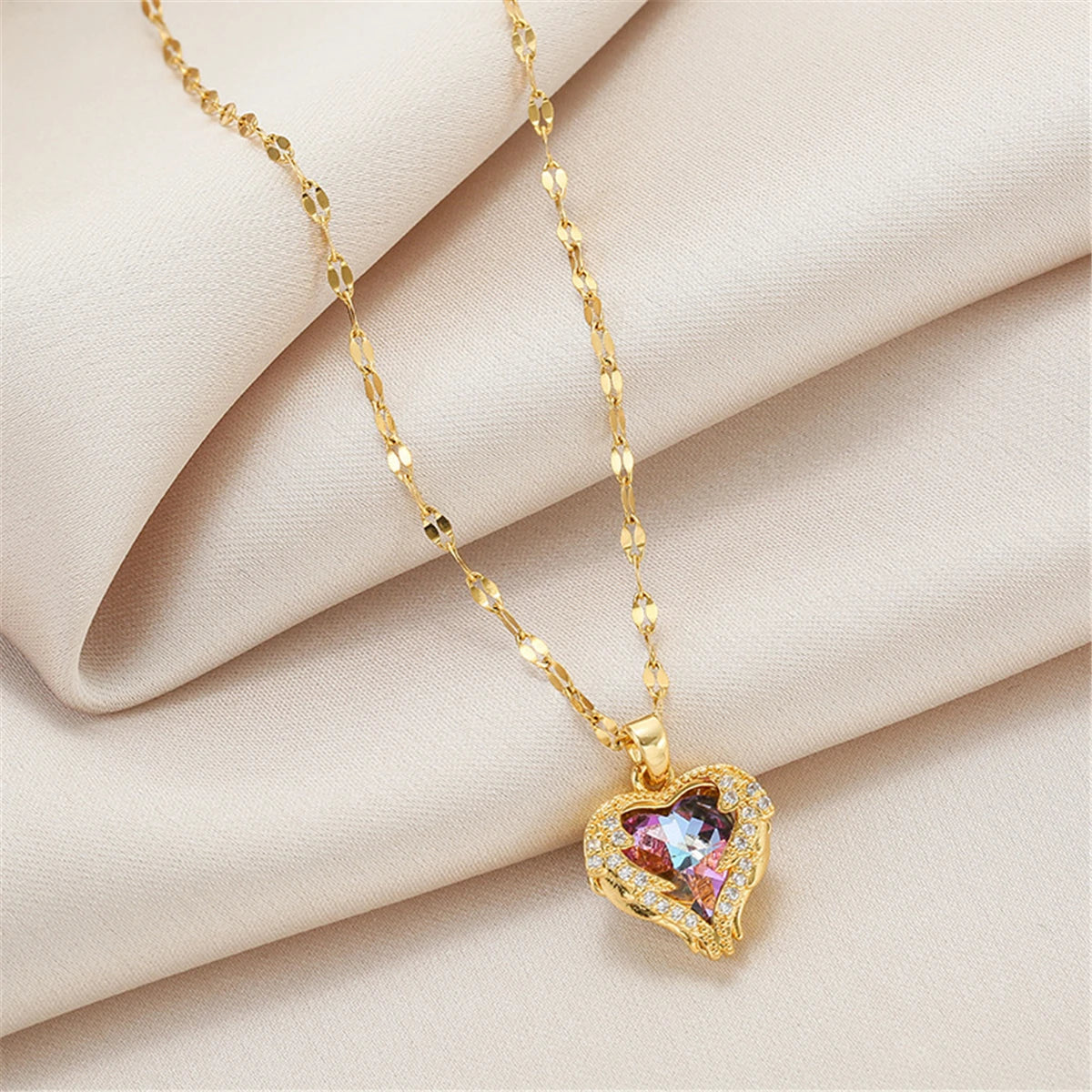 Collier en chaîne doré avec un pendentif cœur d'océan en cristal coloré sur un tissu beige.