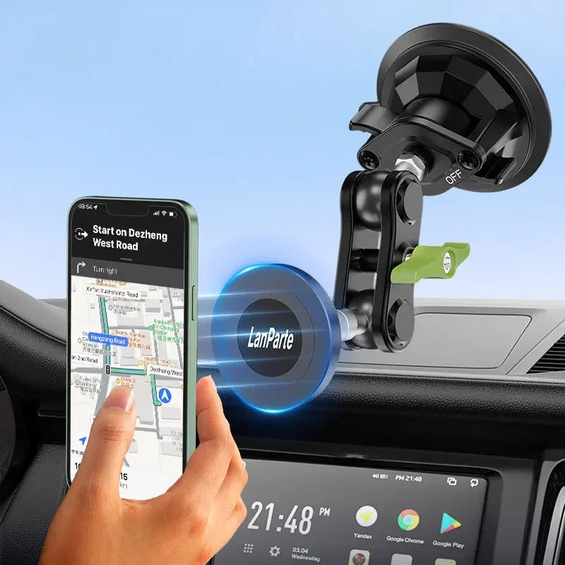 A hand holds a smartphone displaying a map, positioned near a black magnetic car phone mount.