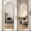 A full length oval wall mirror with a black frame reflects a modern living room interior.