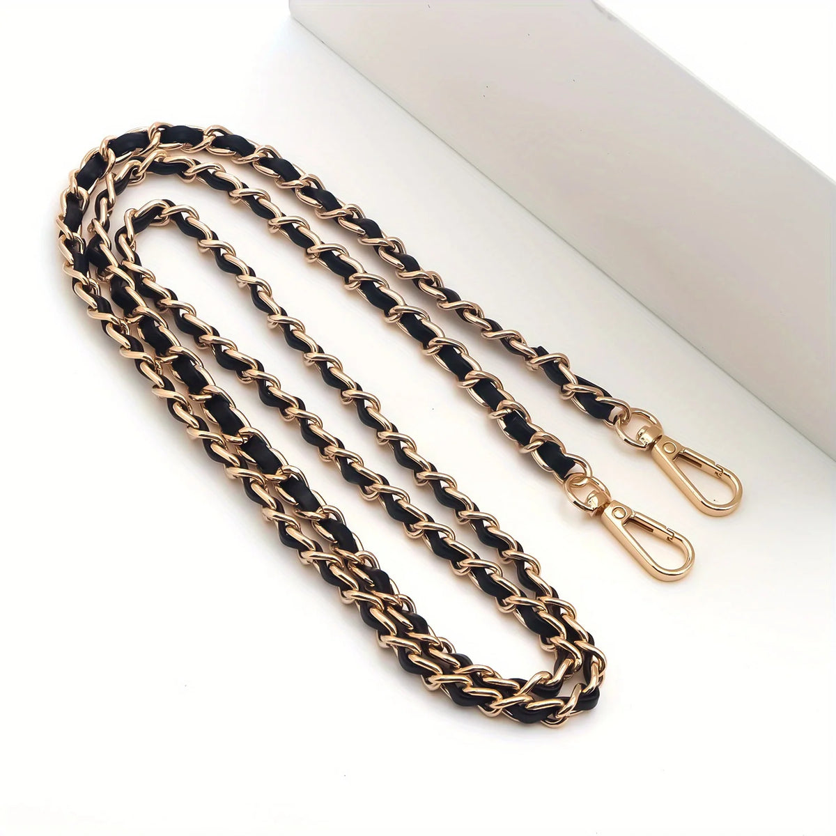 A gold-toned metal chain purse strap with a black leather cord and a secure clasp.