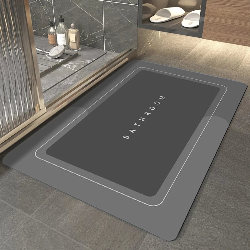 A rectangular gray bath mat with the word BATHROOM embossed on it, placed on a tiled floor.