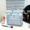 A light blue and white checkered travel makeup bag with a wide opening is displayed on a white surface.