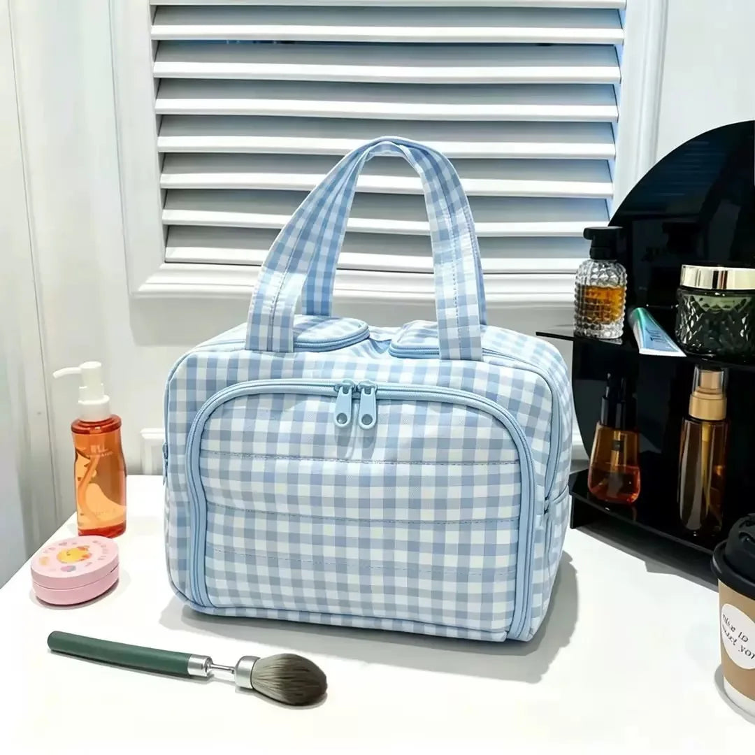 A light blue and white checkered travel makeup bag with a wide opening is displayed on a white surface.