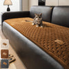 A tabby cat sitting on a brown quilted plush sofa cover with a dark leather frame.