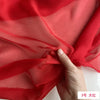 A hand is folding a piece of sheer red silk chiffon fabric, showcasing its lightweight and translucent quality.