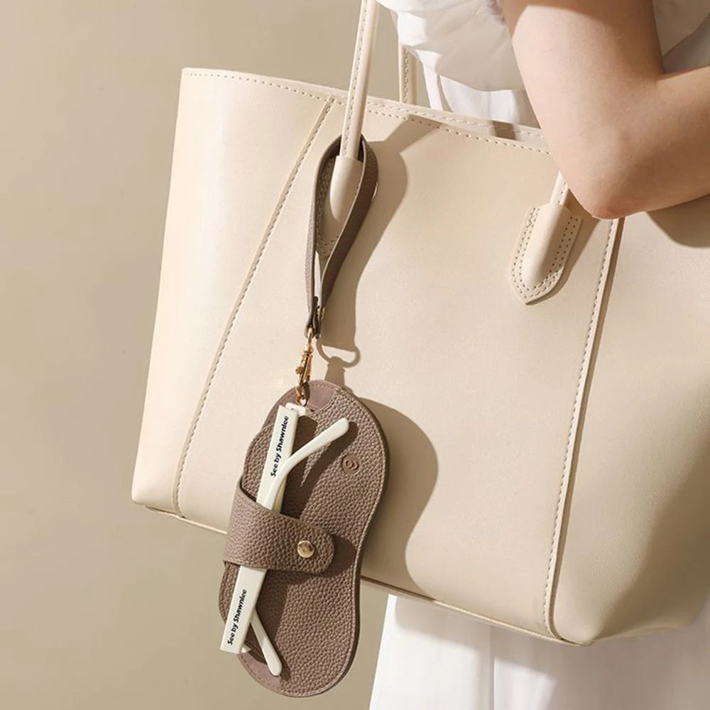 A beige leather handbag with a tan strap and a matching glasses case hanging from it.