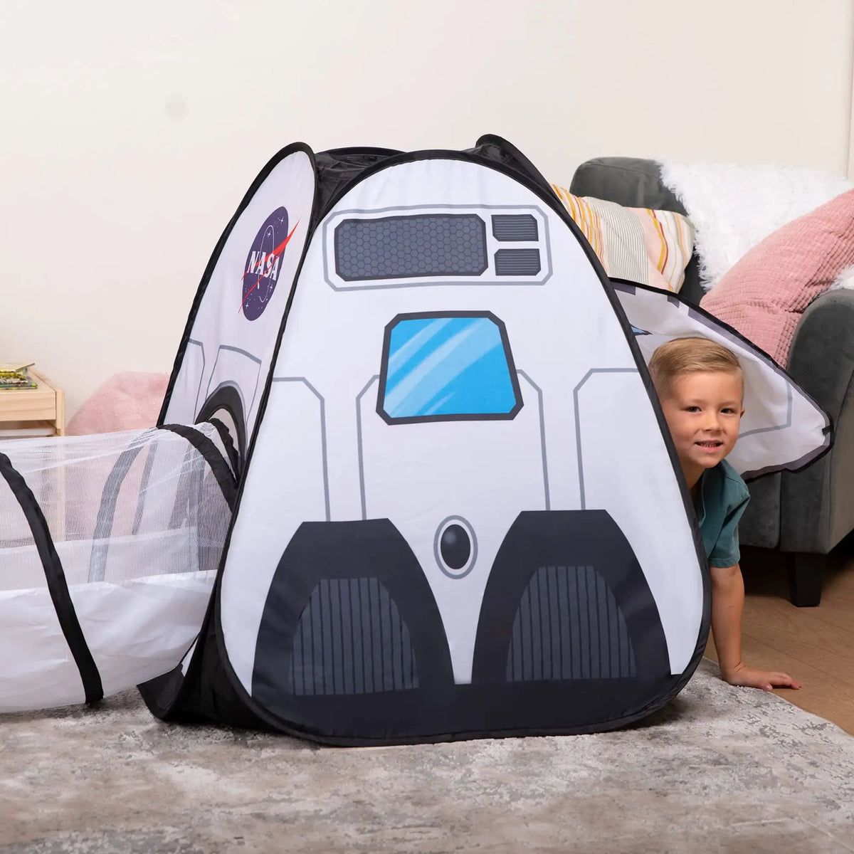 A child is smiling next to a black and white rocket ship play tent set with a tunnel and cube tent.