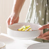 A hand is holding a white ceramic soup bowl filled with yellow salad and rice, set against a light background.