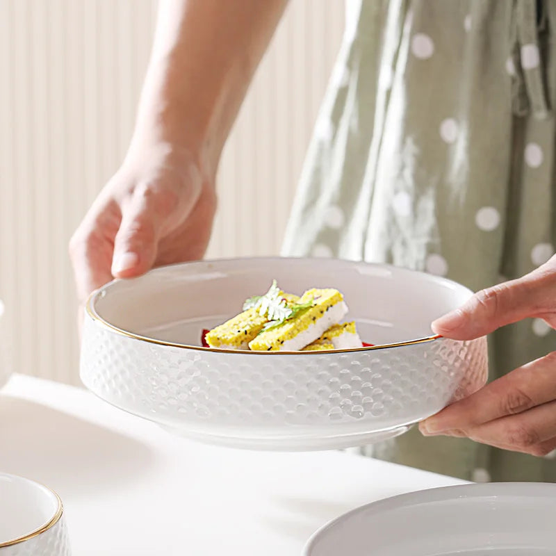 A hand is holding a white ceramic soup bowl filled with yellow salad and rice, set against a light background.