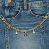 A close-up of a gold alloy chain with pearl and bow decorations attached to a denim jean pocket.