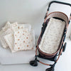 A brown stroller with a white cushion and several folded light-colored fabric items are displayed on a white surface.