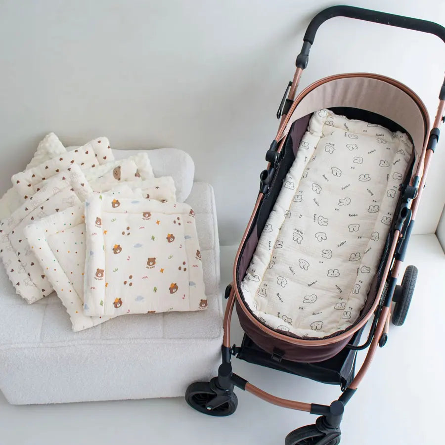 A brown stroller with a white cushion and several folded light-colored fabric items are displayed on a white surface.