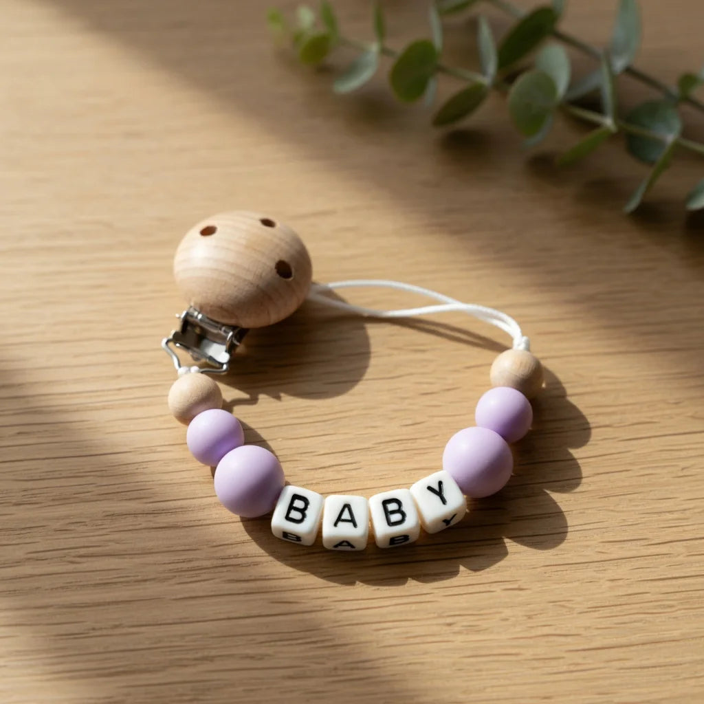 A wooden pacifier clip featuring purple beads and the name BABY carved into small wooden pieces.