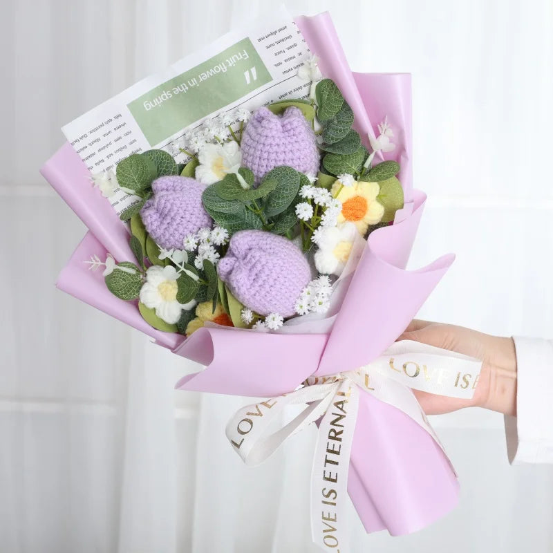 Ein Strauß handgefertigter Häkelblumen in lila und grün, eingebettet in rosa Papier