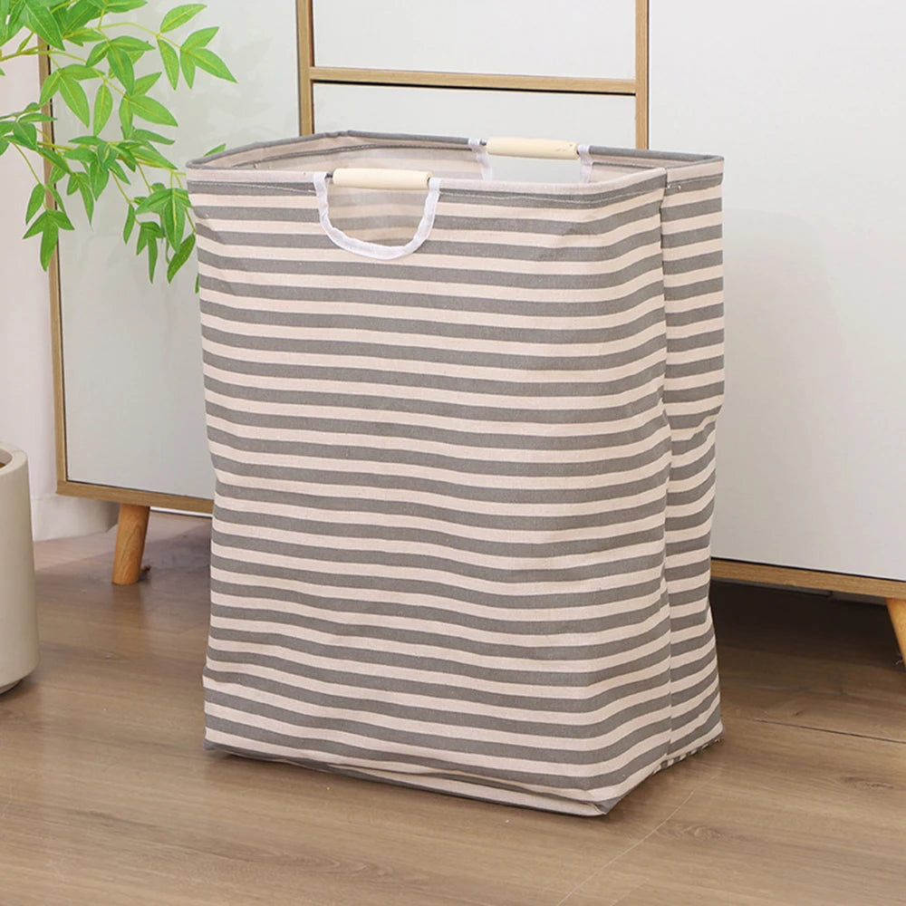A striped beige and gray foldable waterproof laundry basket with handles standing on a wooden floor.