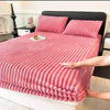 A pink knitted fitted bed sheet is laid out on a black bed with a headboard.