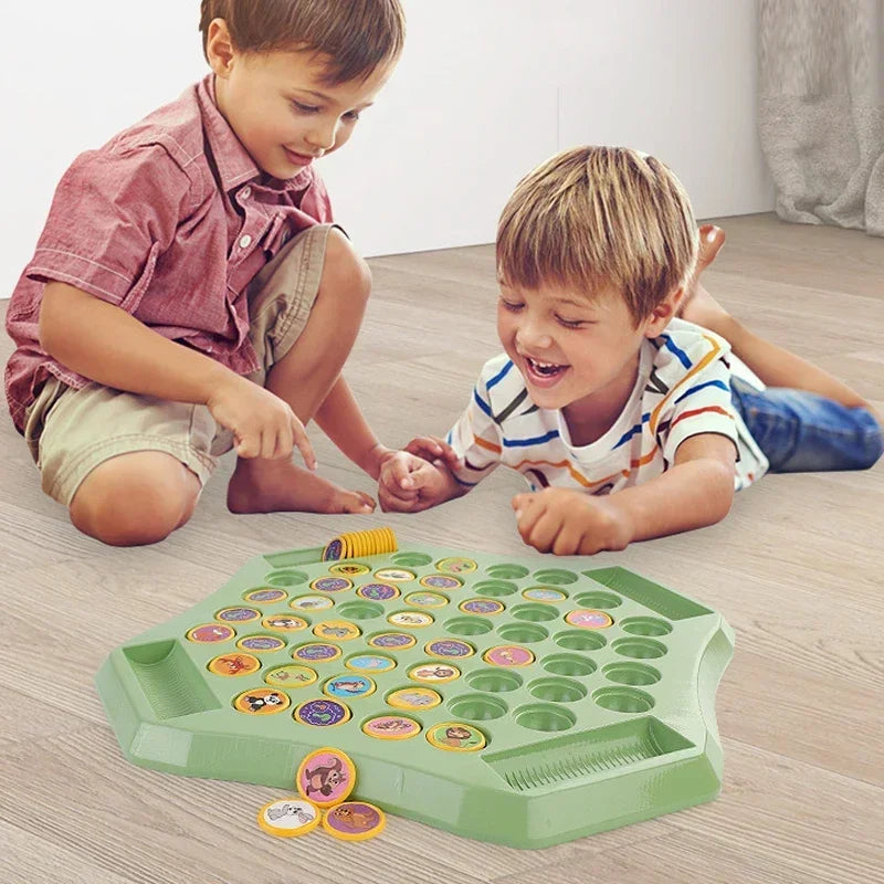 Three young children playing with a green flip chess game on a wooden floor.