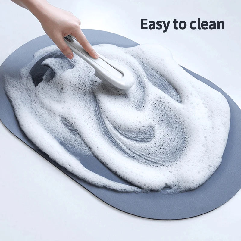 A hand is cleaning a gray bath mat with a white sponge, demonstrating its easy to clean feature.