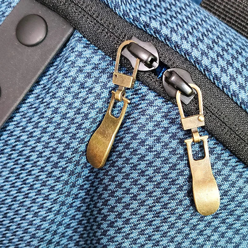A close-up of a brass metal zipper pull replacement slider attached to a black strap on a blue plaid fabric.