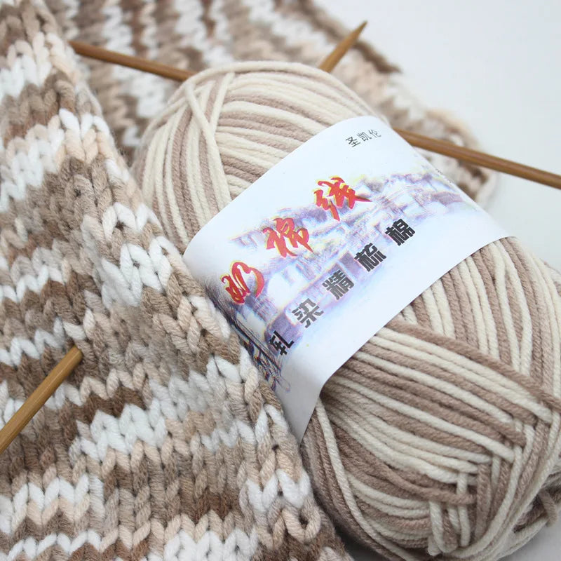 A ball of beige milk cotton blend yarn with a white label and wooden knitting needles is shown.