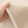 A hand is holding a beige geometric sofa cushion cover, showing the textured fabric and stitching.