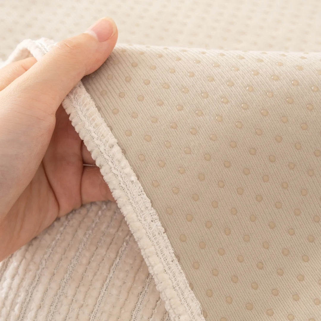 A hand is holding a beige geometric sofa cushion cover, showing the textured fabric and stitching.