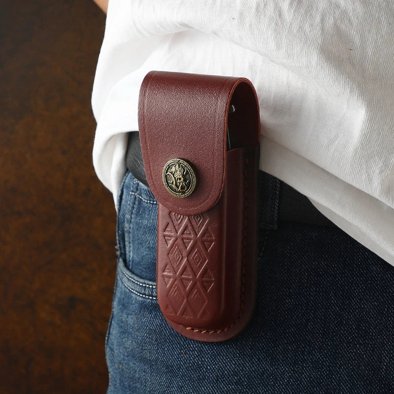 A brown leather folding knife case is shown against a white shirt and denim jeans.