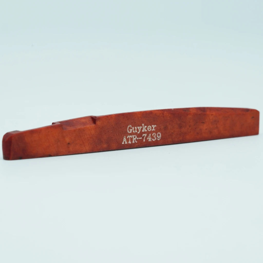 A wooden acoustic guitar bridge saddle with the name Guyker ATR-7439 engraved on it.