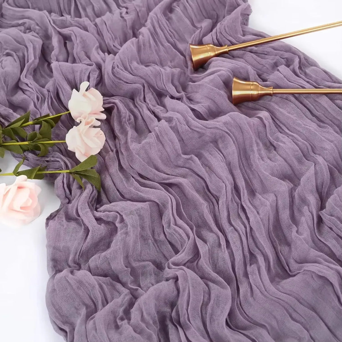 A purple cotton gauze table runner with ruffled texture, gold-toned metal utensils, and pink floral accents.