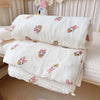White muslin baby blanket with pink floral designs folded on a white surface.