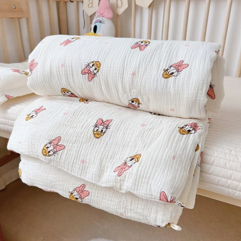 White muslin baby blanket with pink floral designs folded on a white surface.