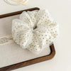 A white polka dot mesh scrunchie hair tie is displayed on a wooden tray.