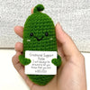 Handcrafted pickle plush with a green fuzzy body and simple black eyes, held in a person's hand.