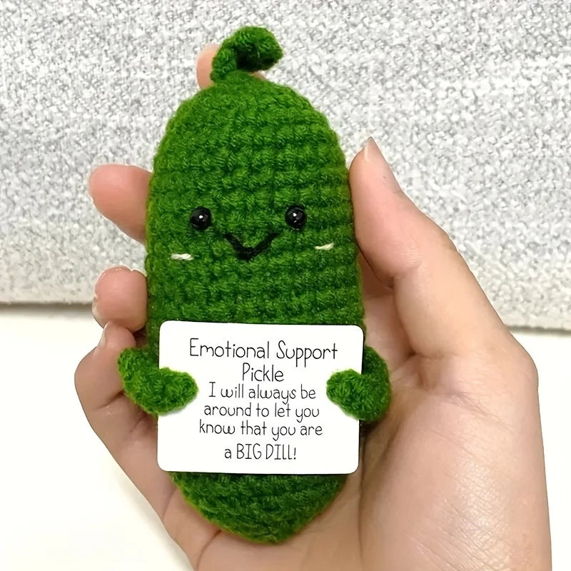 Handcrafted pickle plush with a green fuzzy body and simple black eyes, held in a person's hand.