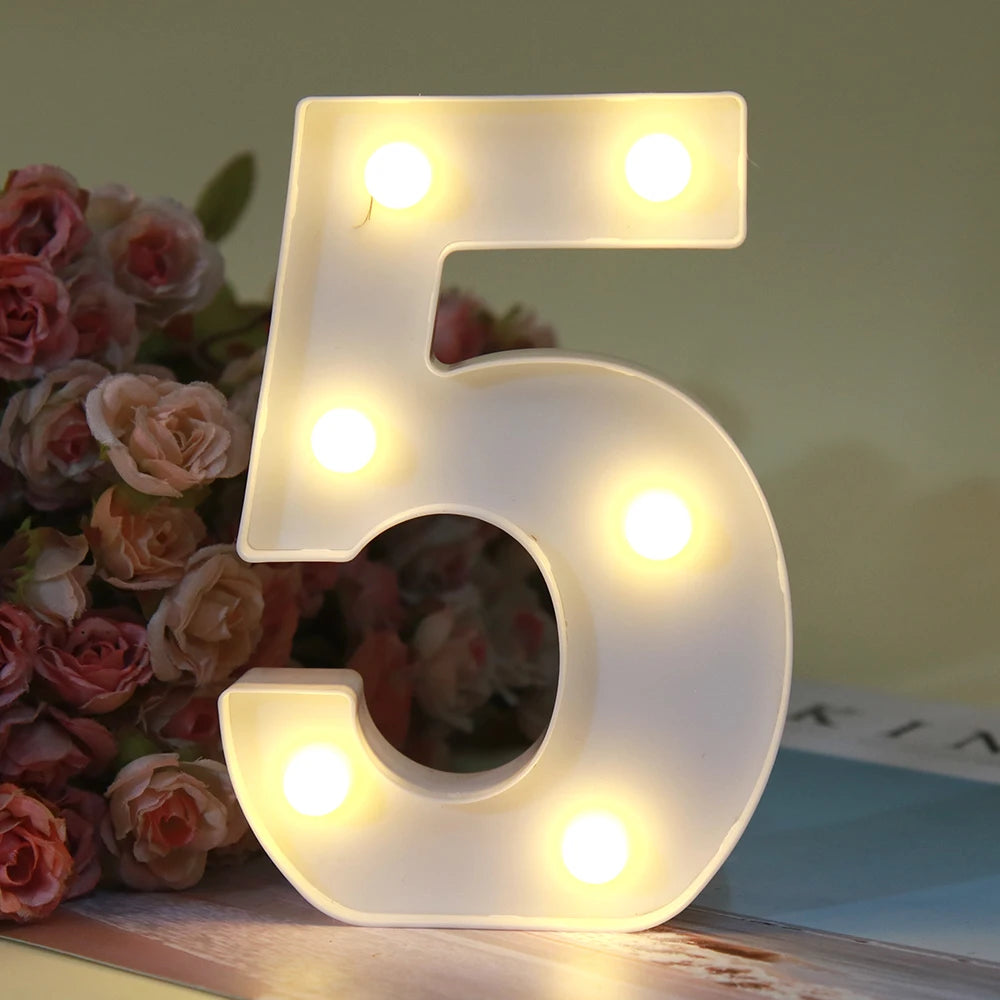 Lumière de nuit alphabétique LED blanche en forme de cinq, posée sur une surface en bois à côté de roses roses.