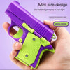 A hand holds a purple and lime green mini pistol toy designed for stress relief.