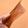 A hand holds an ultra-thin brown leather passport holder with card slots.