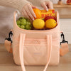 A light peach insulated reusable lunch bag filled with fresh fruit, being held by a person's hands.