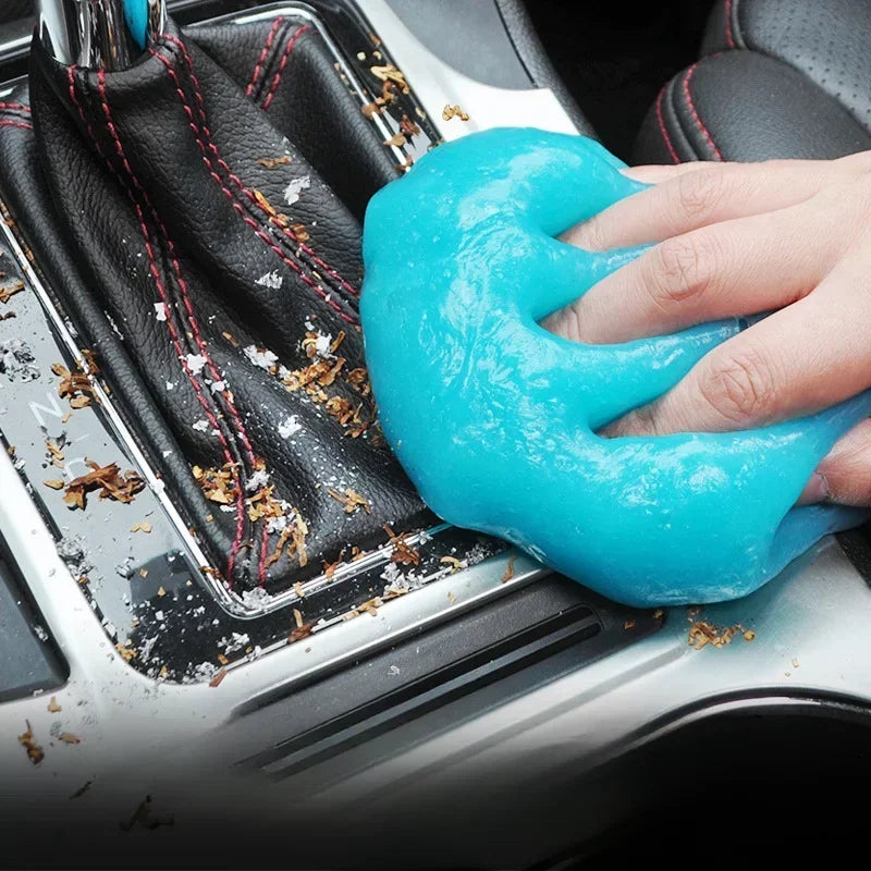 A hand applies a bright blue reusable cleaning gel to the interior of a car, targeting hard-to-reach gaps.