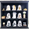 A display of various white ghost-shaped figurines depicting cats and other animals in a dark wooden shelf.
