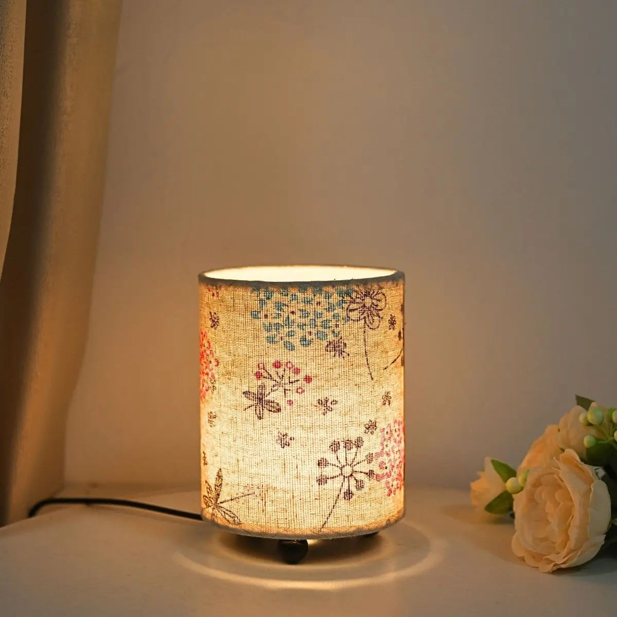 A cylindrical fabric desk lamp with a warm glow featuring a floral pattern.
