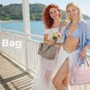 Two women standing on a boardwalk by the sea holding and displaying a puffy tote bag
