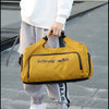 A person is holding a yellow duffel bag with a shoe pocket in an outdoor setting.