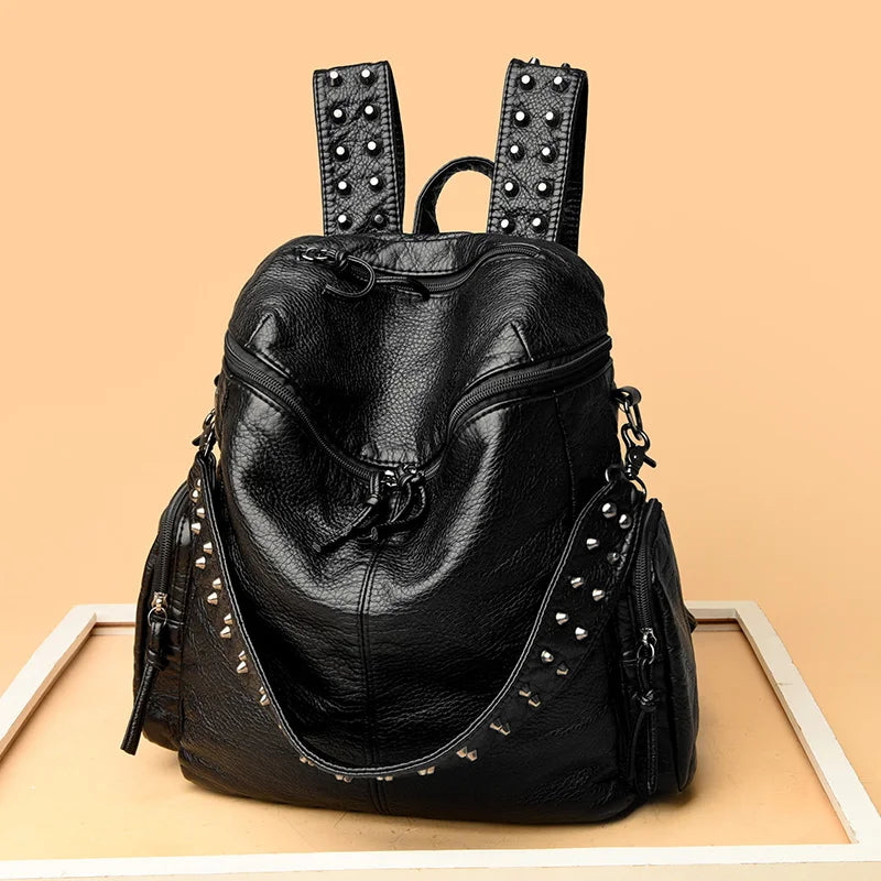 Black soft leather backpack with silver rivets and studs displayed on a light wooden surface.