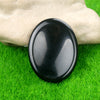 A smooth, black oval crystal stone resting on vibrant green grass, held by a hand.
